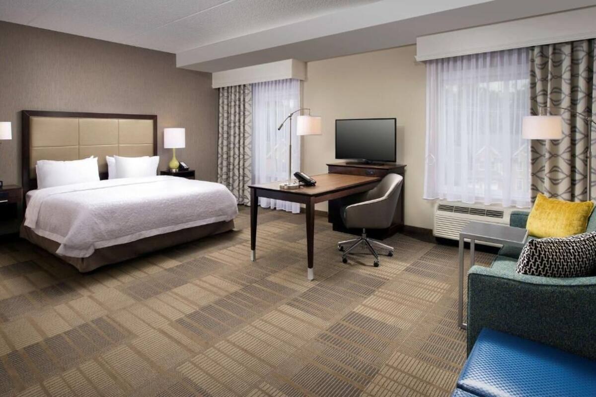 A hotel room with a large bed, a desk with a chair, a television, and a sofa.