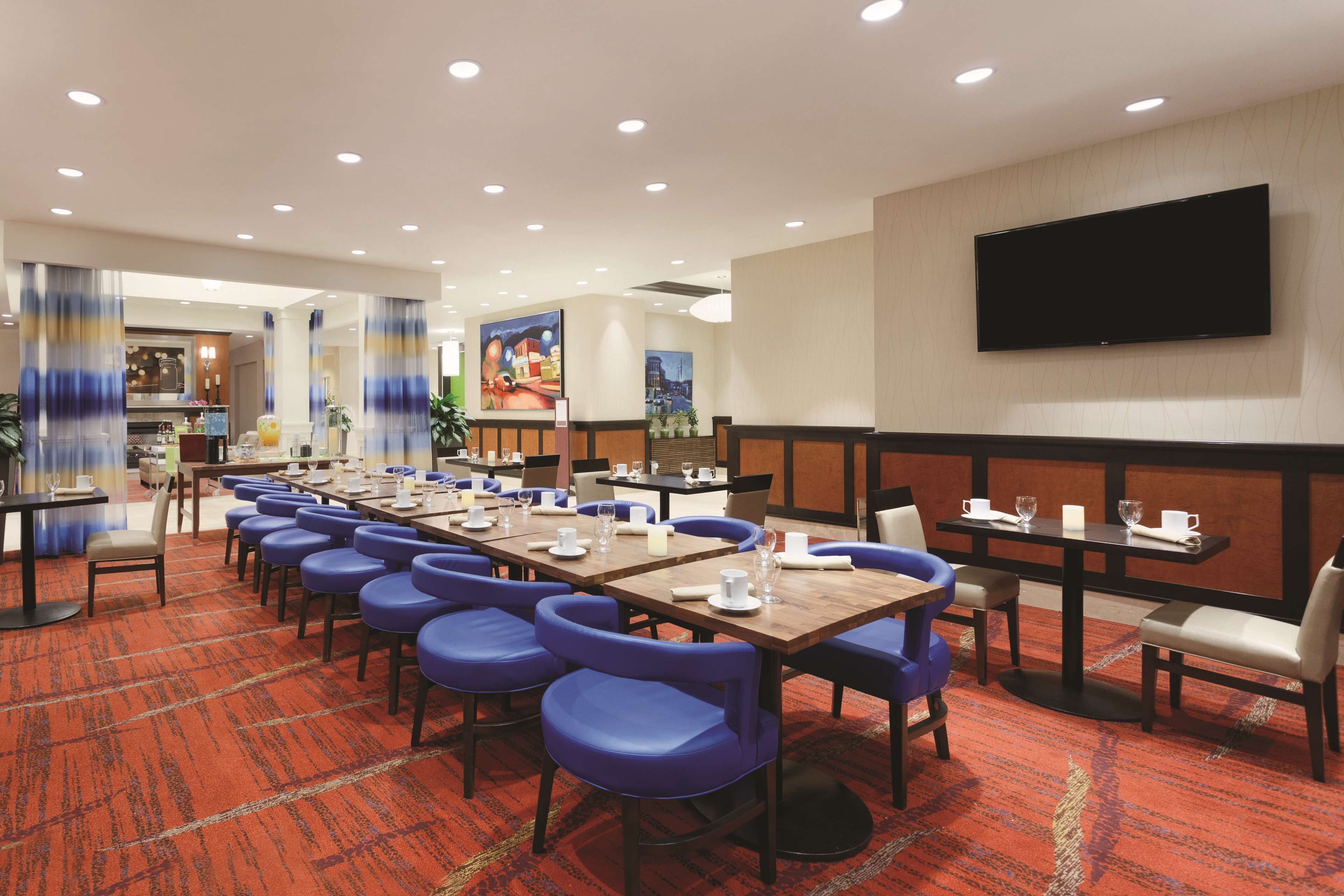 A conference room with a long table, blue chairs, and a flat-screen TV on the wall.
