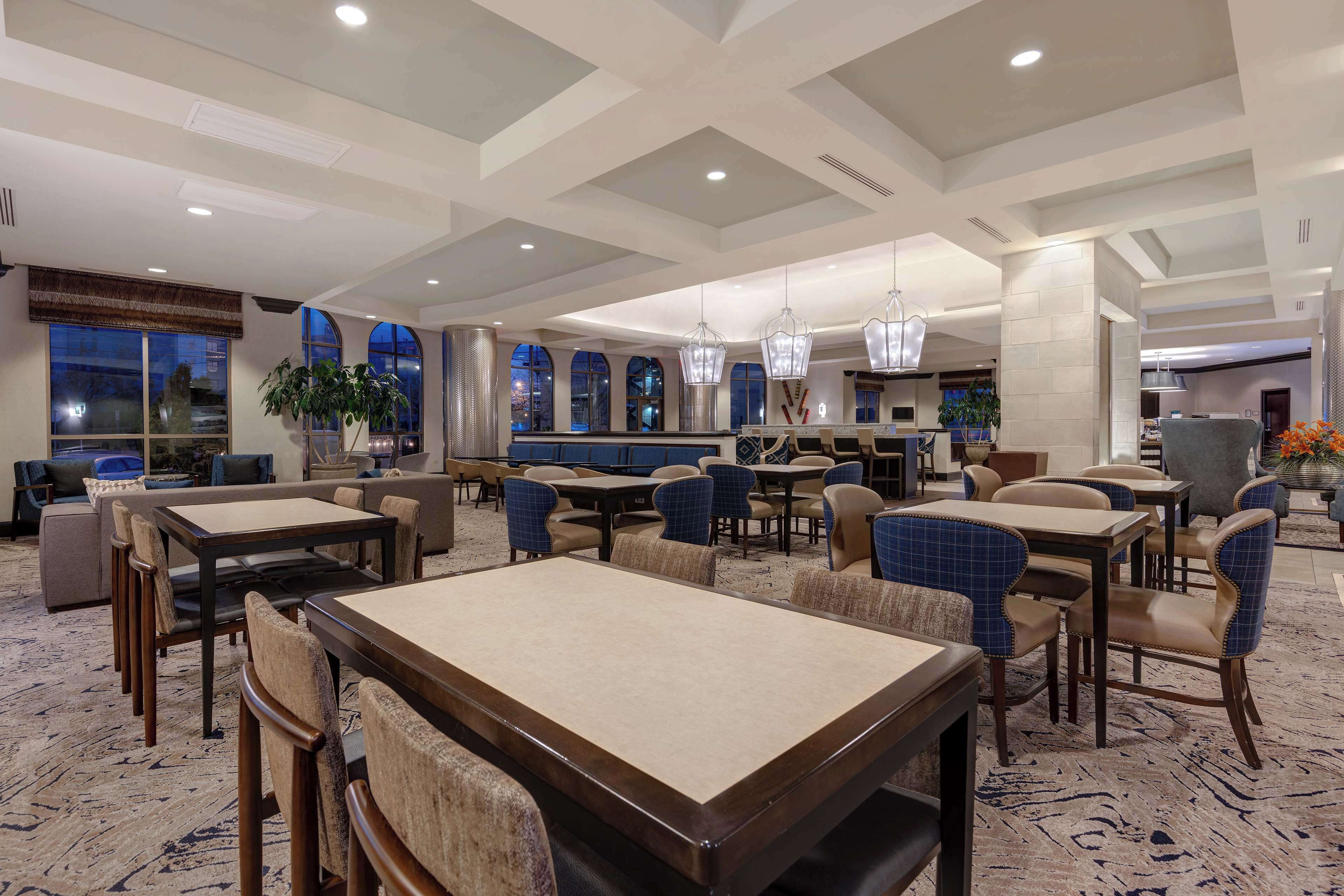 A spacious hotel lobby with multiple dining areas, large windows, and modern lighting fixtures.