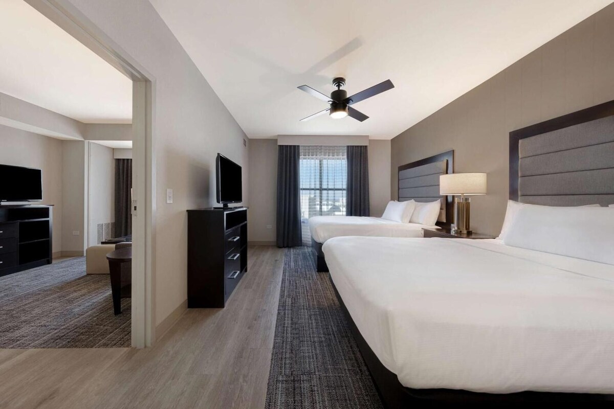 Habitación de hotel con dos camas, televisor, ventilador de techo y vista a la ciudad.