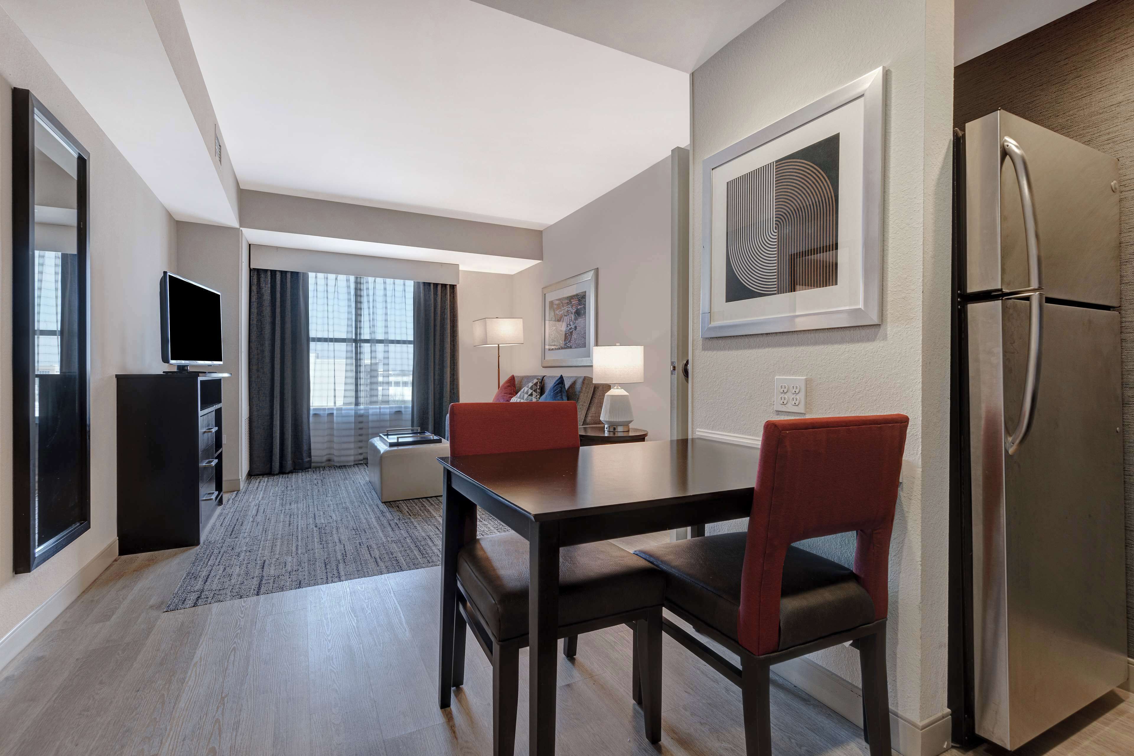 A hotel room with a dining area, a refrigerator, a television, and a window with curtains.