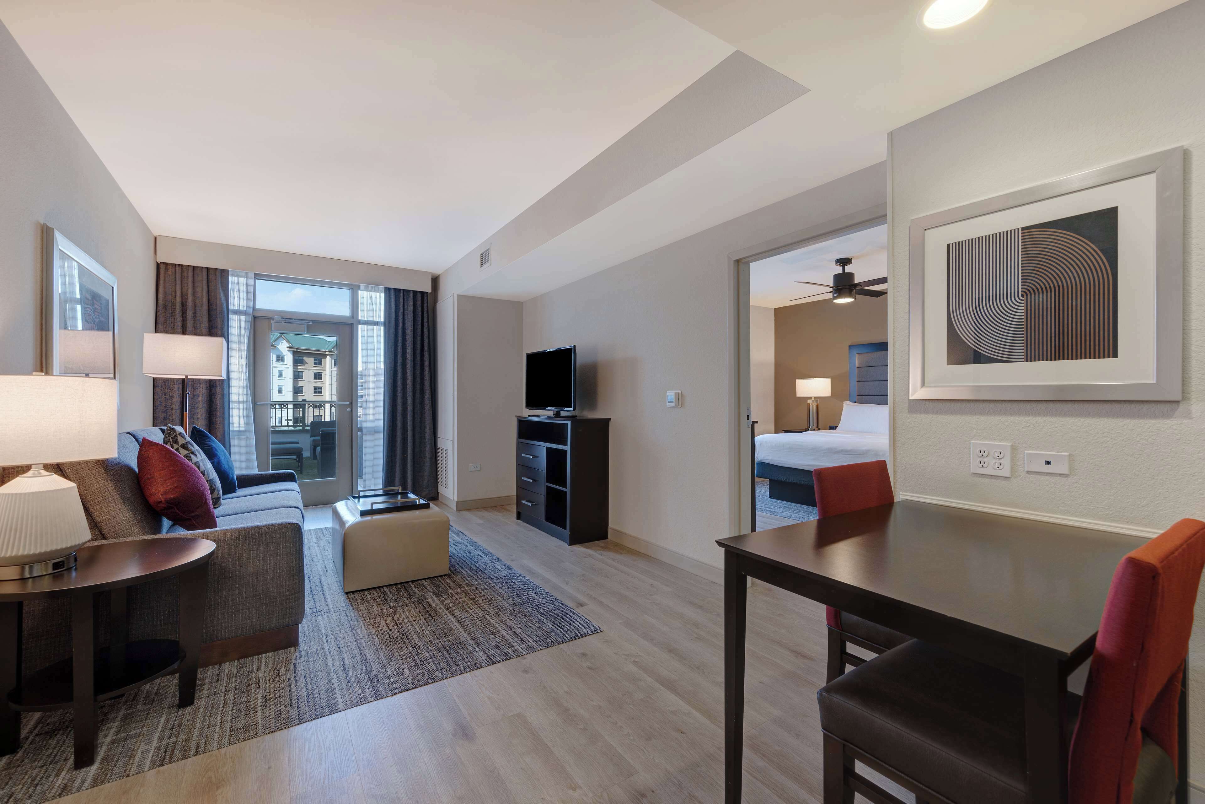 Una habitación de hotel moderna con sofá, una mesa de comedor, televisor y un ventanal con vistas a la ciudad.