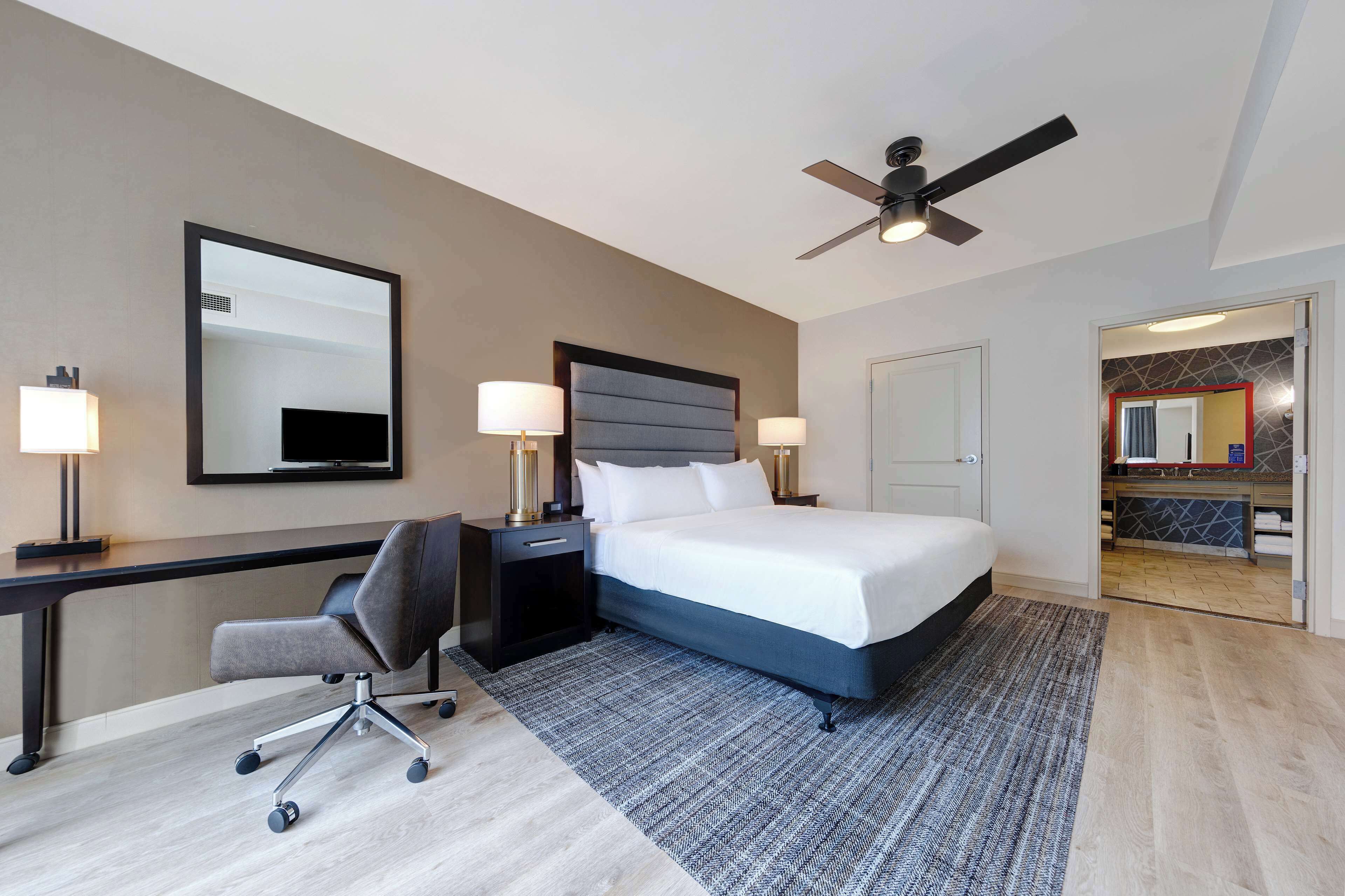 Une chambre d’hôtel équipée d’un lit, d’un bureau, d’une chaise et d’un ventilateur de plafond.