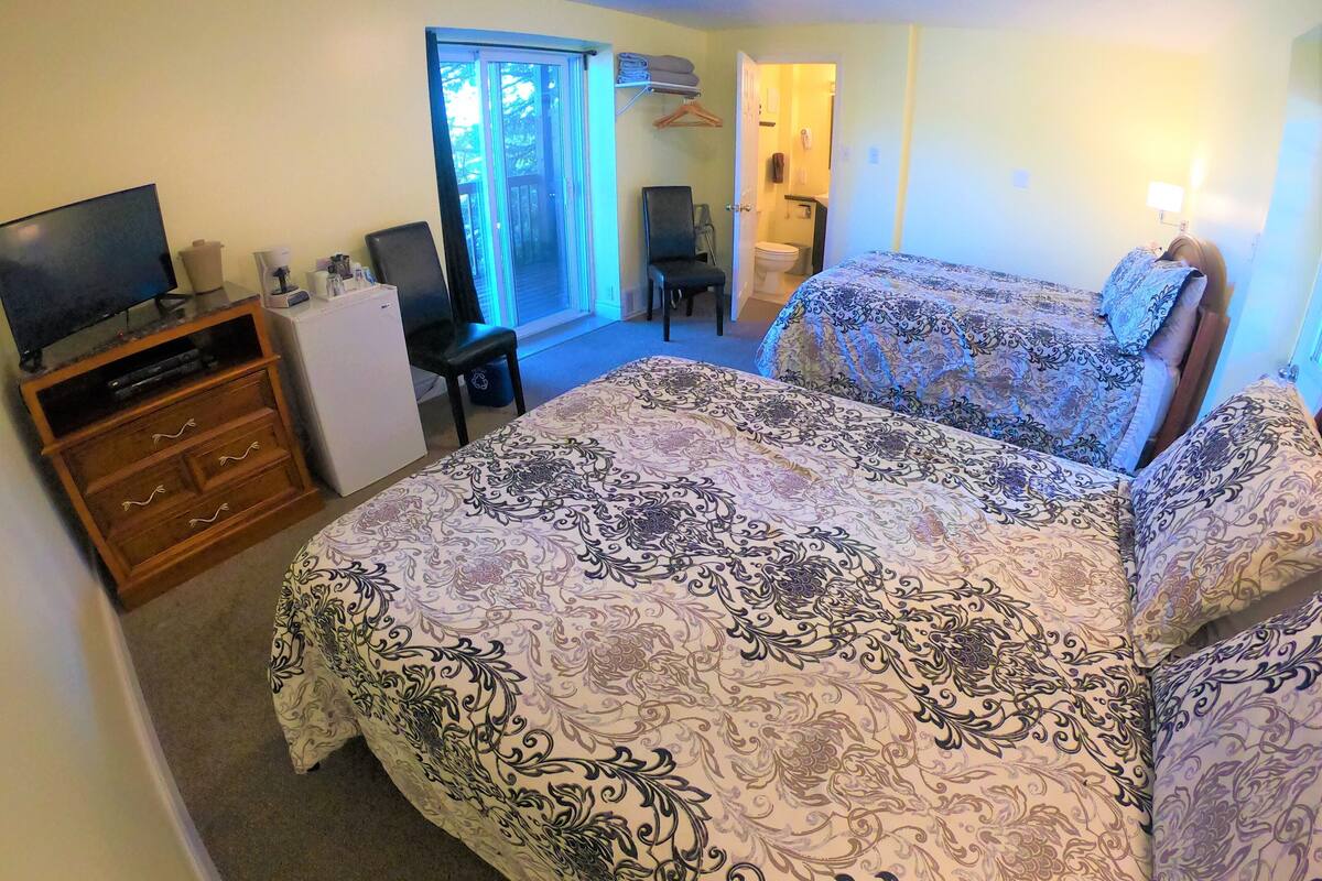 A bedroom with a bed, a desk, a television, and a window.