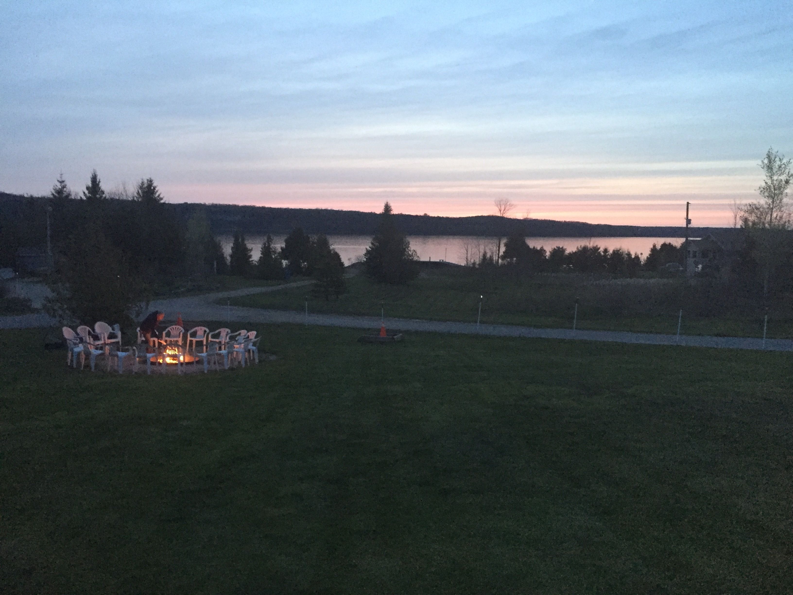 A grassy area with outdoor seating and a view of a lake at dusk.