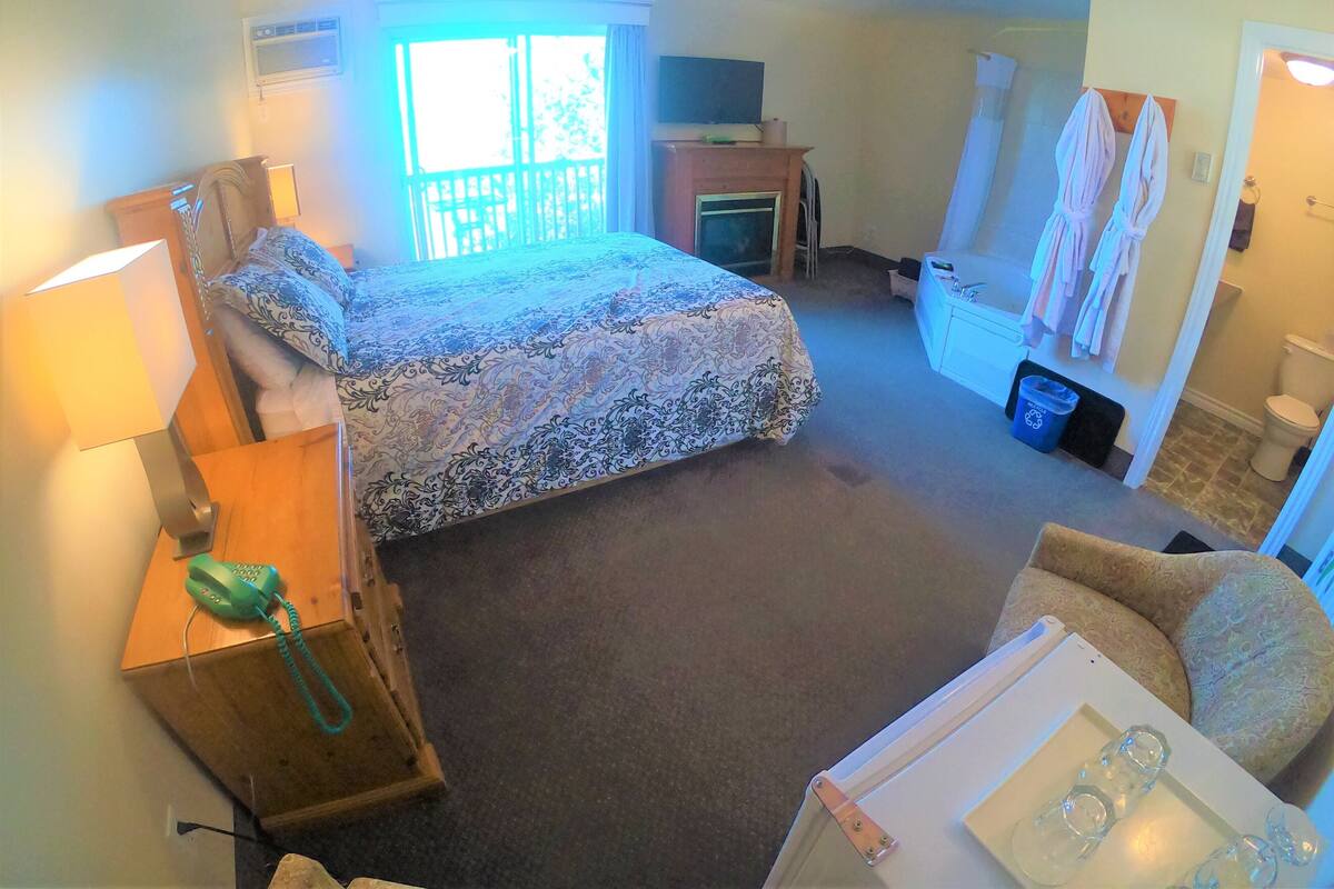 A bedroom with a bed, a desk with a lamp, a chair, a bathroom with a toilet and sink, and a ceiling fan.