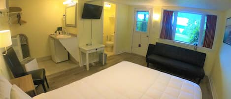 A hotel room with a bed, a desk, a chair, a TV, a window, and a bathroom.