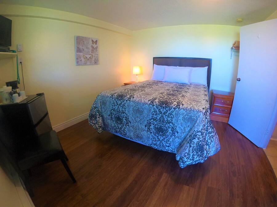 A bedroom with a bed, a desk, a chair, a nightstand, and a wall-mounted lamp.