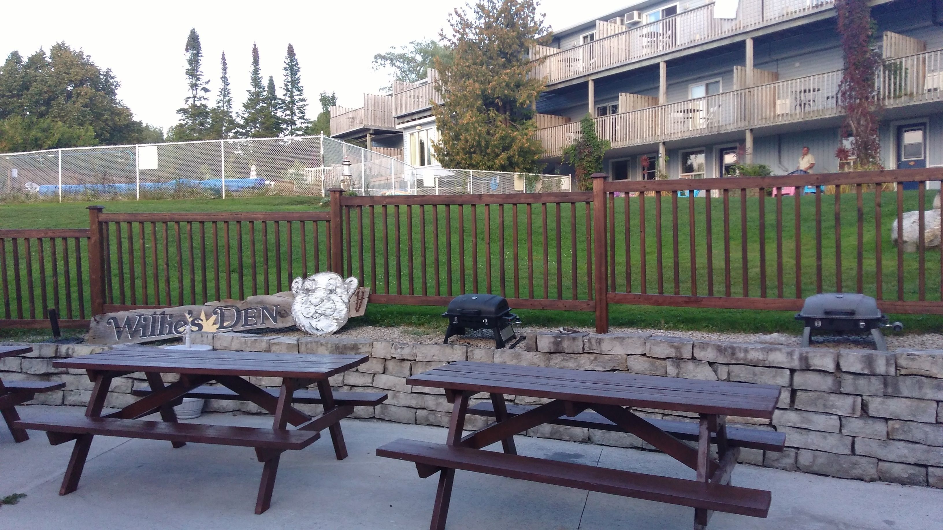 A patio area with picnic tables, a barbecue grill, and a wooden fence.