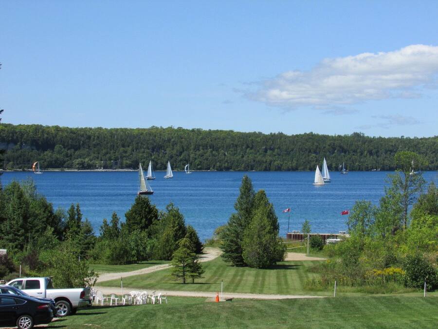 Une vue sur un lac où l’on voit des voiliers, entouré de verdure et bordé d’un terrain de golf.