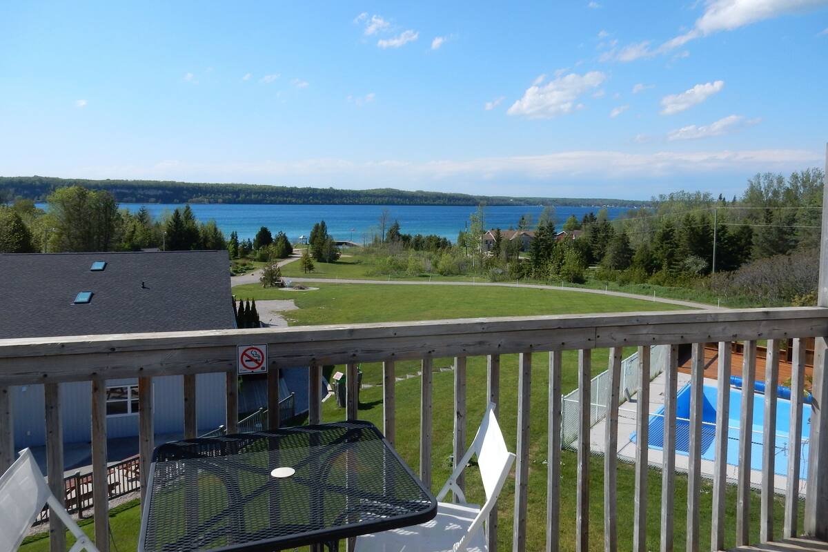 A balcony with a view of a lake, a swimming pool, and a grassy area.