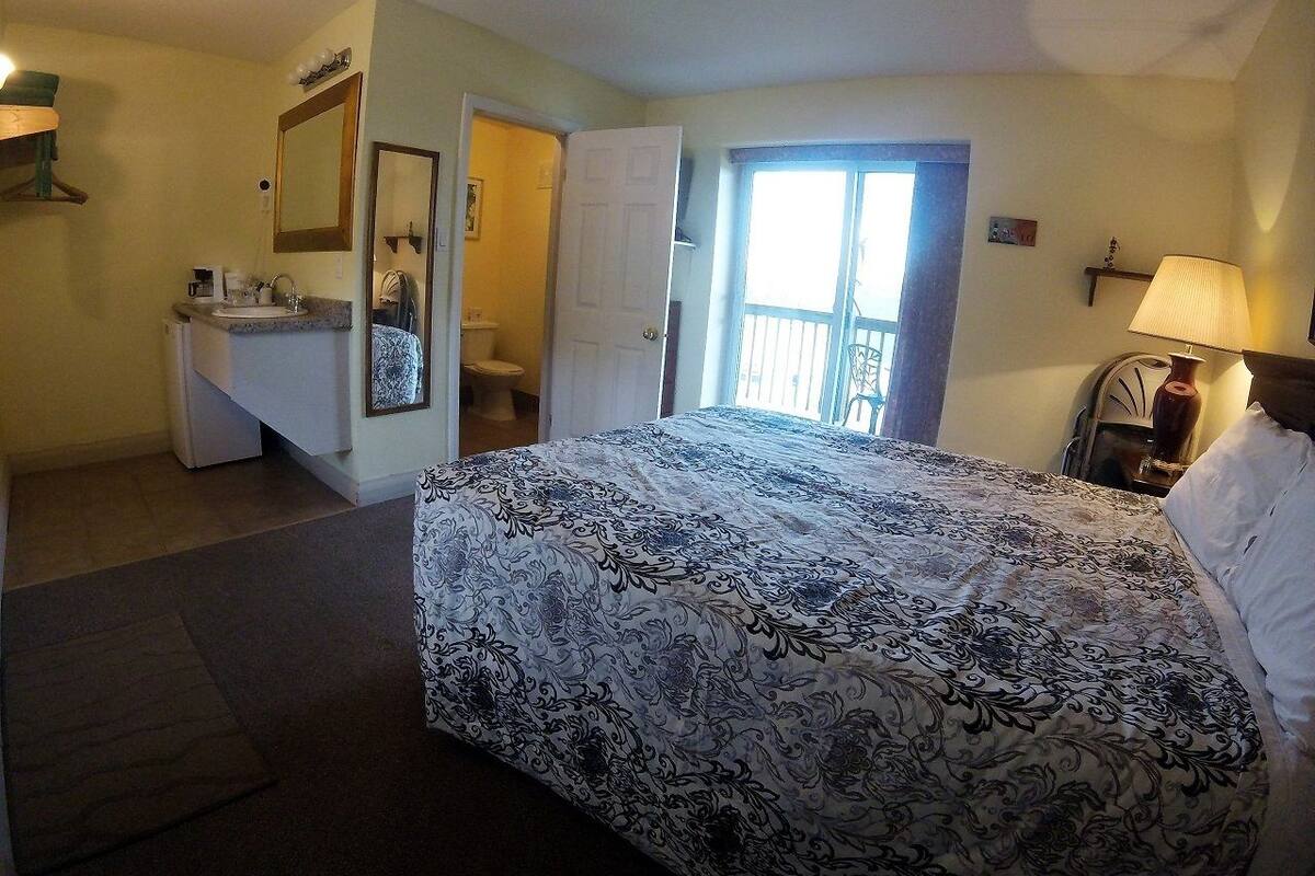 A bedroom with a bed, a dresser, a mirror, a door leading to a balcony, and a lamp.