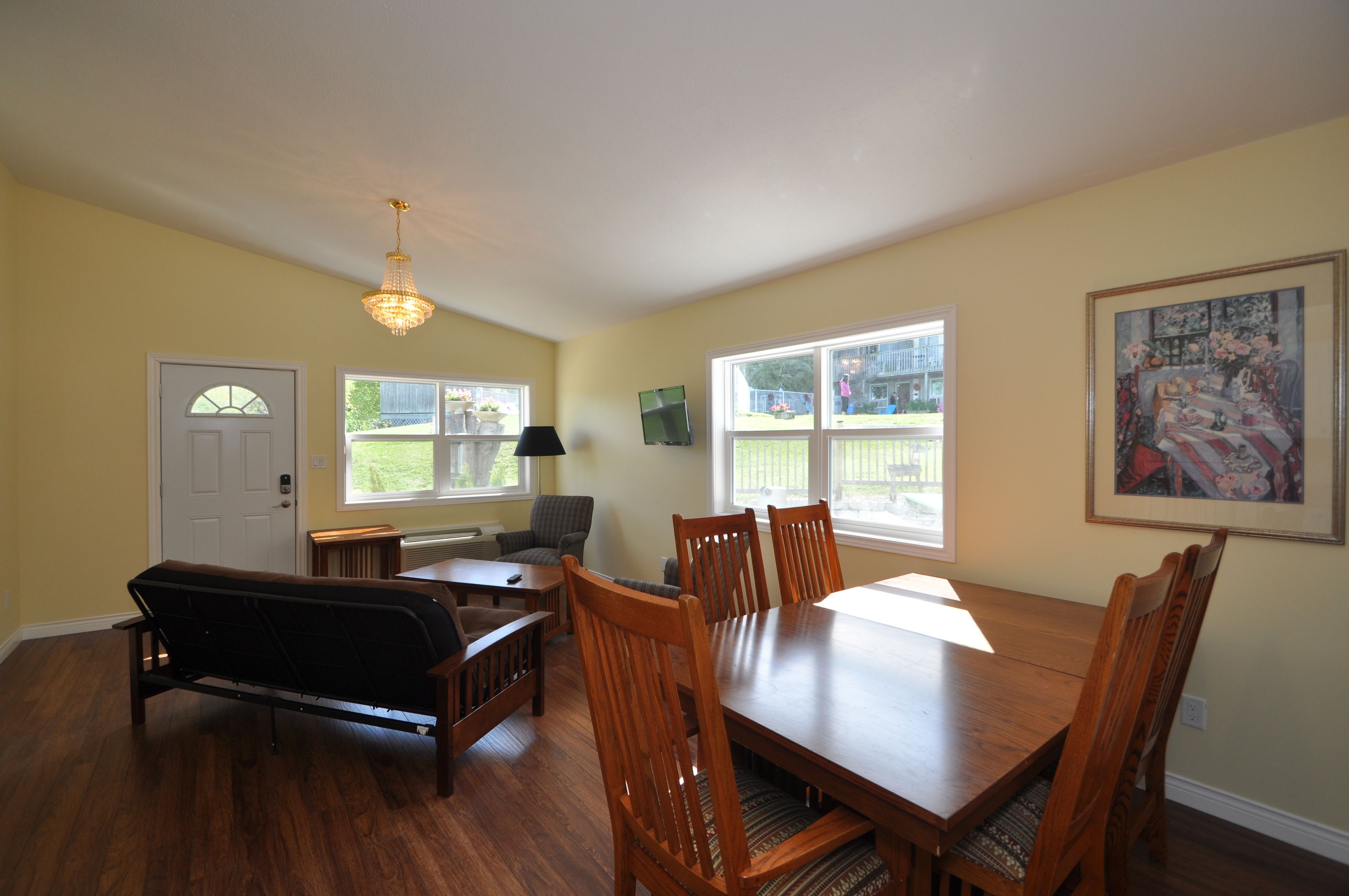 A dining room with a wooden table and chairs, a bench, a chandelier, and a painting on the wall.