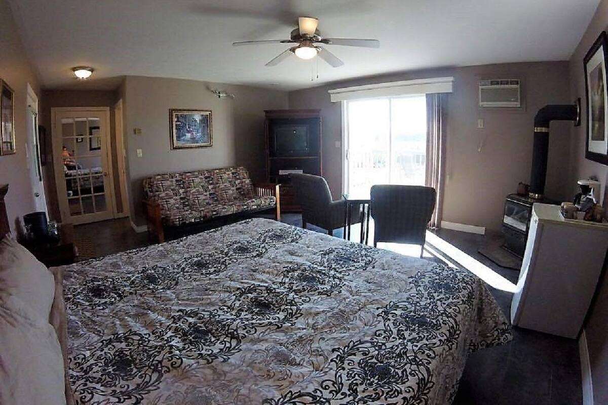 A bedroom with a large bed, a desk, a chair, a television, and a ceiling fan.
