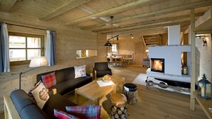 Interior acogedor de una cabaña con techo de madera, chimenea, sofá, mesa de comedor y zona de cocina.