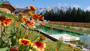 Una cabaña en la montaña con piscina y flores al frente.