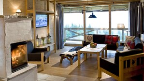 Una sala de estar acogedora con chimenea, muebles de madera, televisor y ventanas grandes con cortinas.