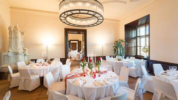 A banquet hall with round tables set for a formal event, featuring white tablecloths, candles, and floral centerpieces.