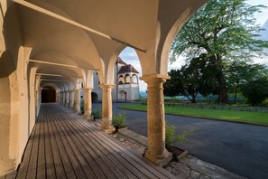 Une allée couverte, bordée de colonnes en pierre, mène à un bâtiment dont le toit est rouge.