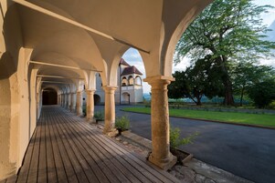 A covered walkway with stone columns, leading to a building with a red roof.