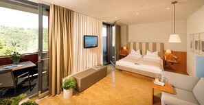 A hotel room with a bed, bedside tables, a desk, a chair, a sofa, a TV, and a balcony with curtains. - Schloss Seggau (Leibnitz)