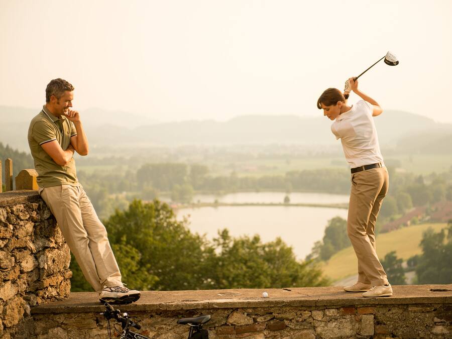 Two people on a stone wall overlooking a lake and hills.