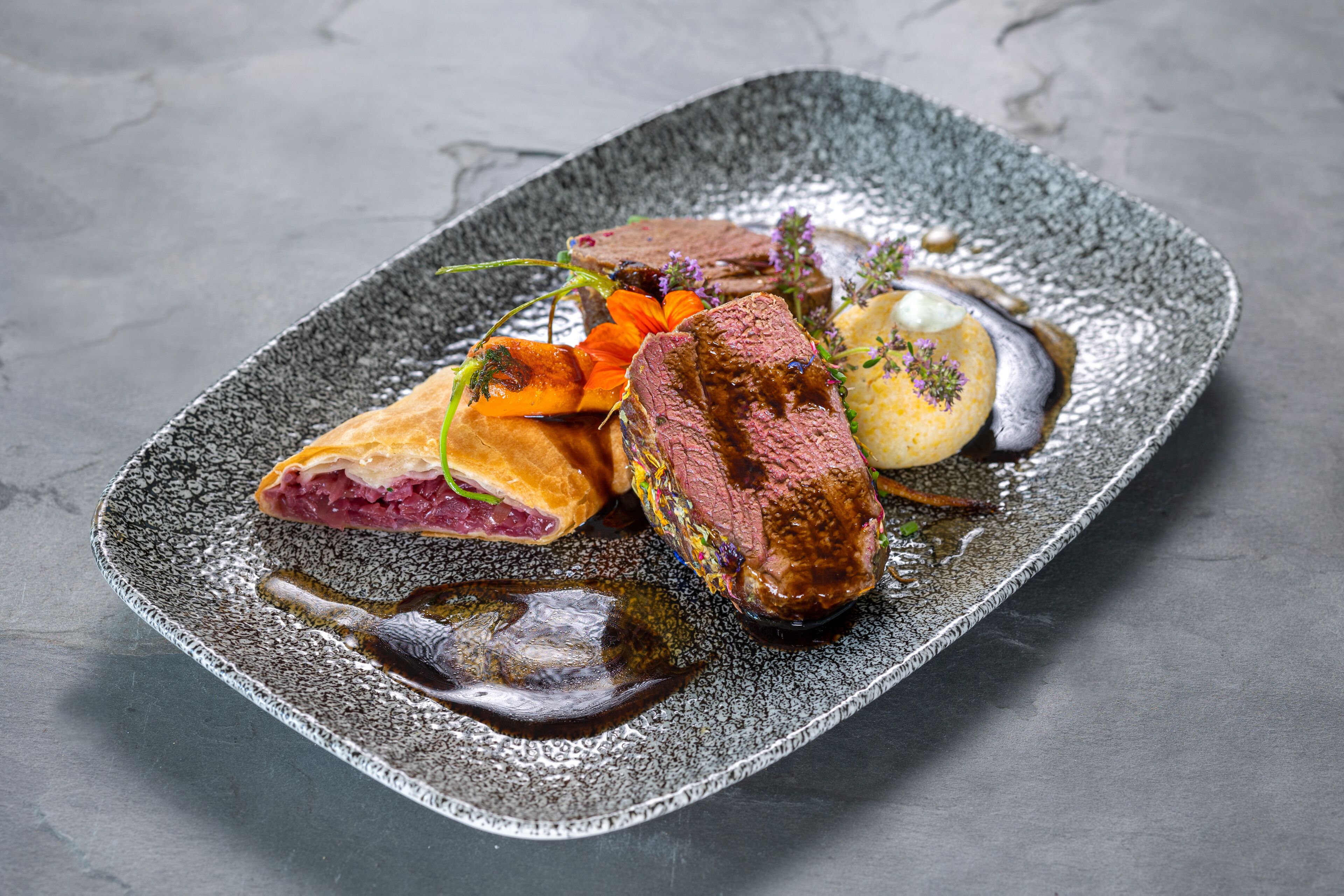 A dish with meat, vegetables, and sauce on a textured plate.