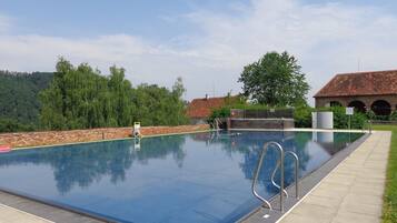 A rectangular swimming pool with a clear blue water surface, surrounded by a stone wall and a paved walkway.