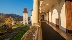 A corridor with a stone column, wooden doors, and a view of a hill with a church. - Schloss Seggau (Leibnitz)