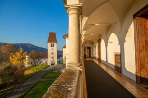 A corridor with a stone column, wooden doors, and a view of a hill with a church.