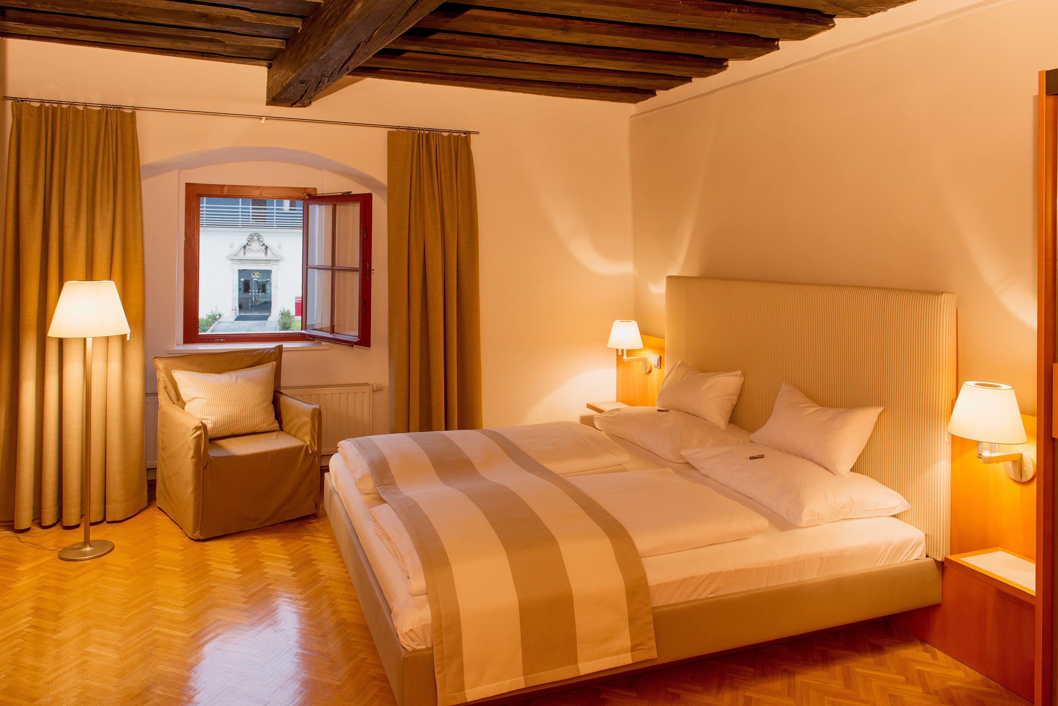 Una habitación de hotel con una cama grande, una silla y vista a un edificio a través de una ventana.