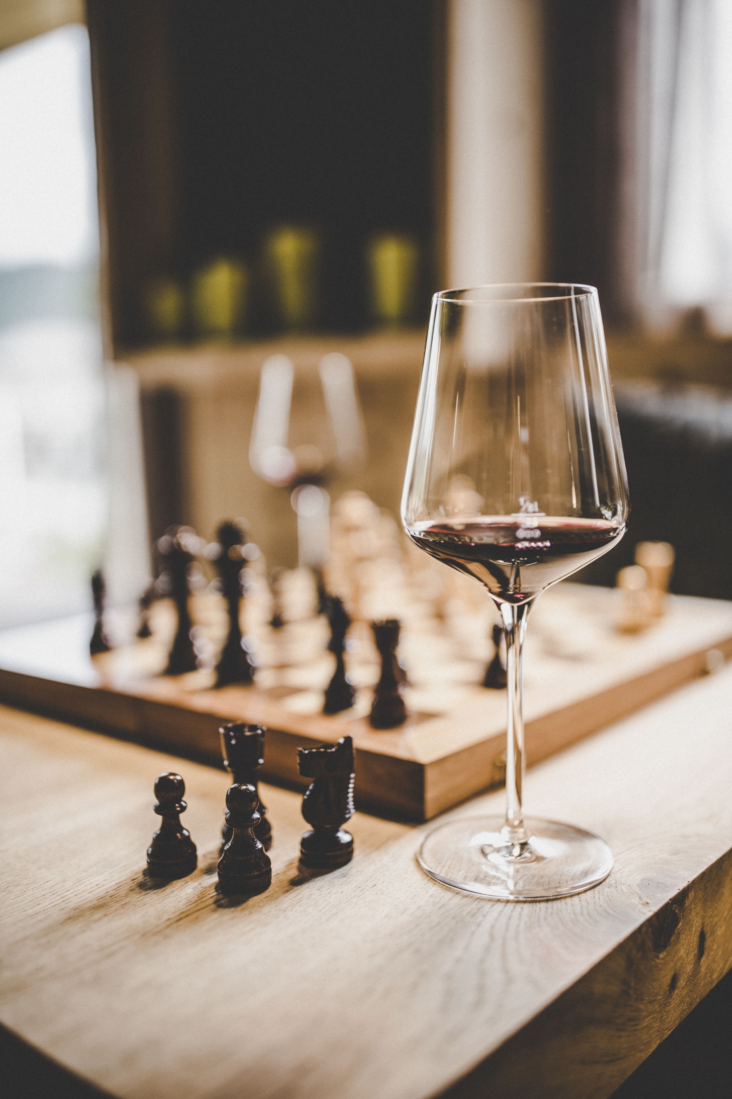 A chessboard with pieces and a wine glass on a wooden surface.