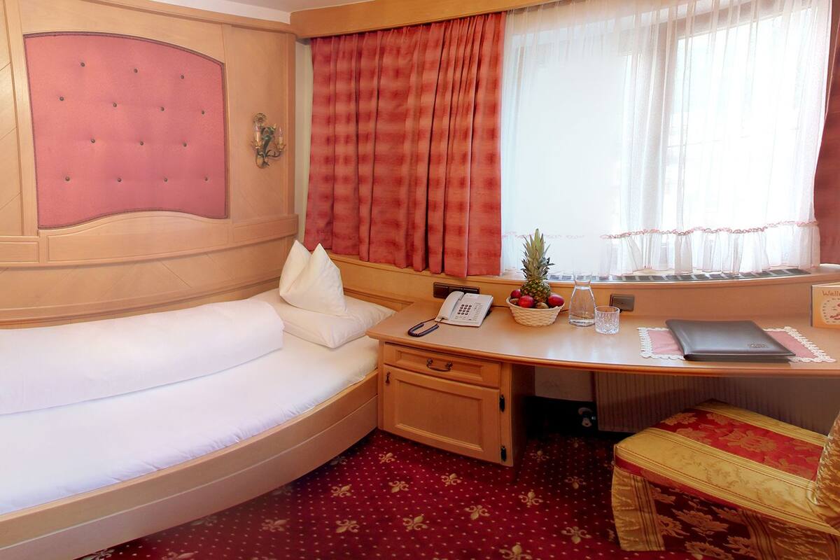 Une pièce confortable avec un lit à la forme arrondie, un bureau avec un téléphone, une petite plante et un panier de fruits.