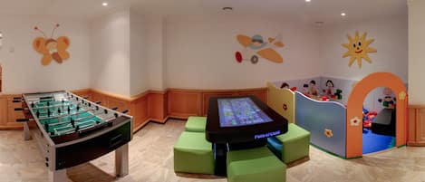 A children's play area with a foosball table, a gaming console, and colorful play structures.