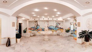 Eine großzügige Lobby mit einer großen Mosaikmalerei, Marmorböden und klassischen architektonischen Elementen.
