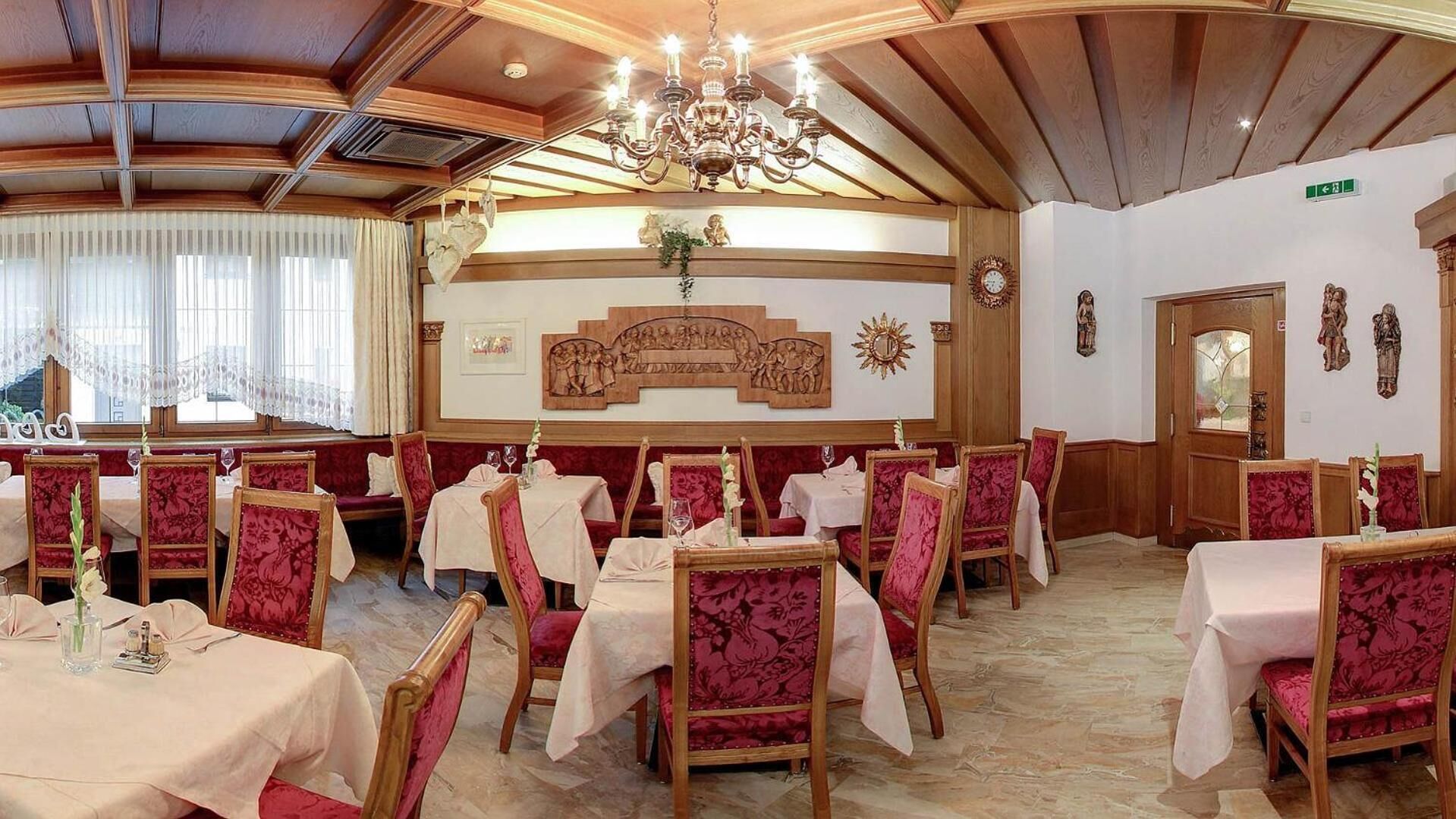 Un espace repas avec des lambris en bois, des lustres et des chaises recouvertes de tissu rouge.