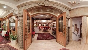 Eine prachtvolle Eingangshalle mit aufwendigen Steinbögen, einer Chandelier und einem Essbereich mit Tischen und Stühlen.