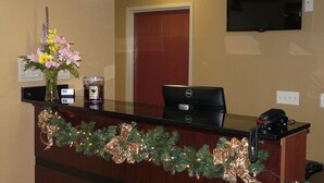 A reception desk with a Christmas garland, a desk lamp, a vase with flowers, and a desk phone. - Cobblestone Inn & Suites - Harper (Harper)