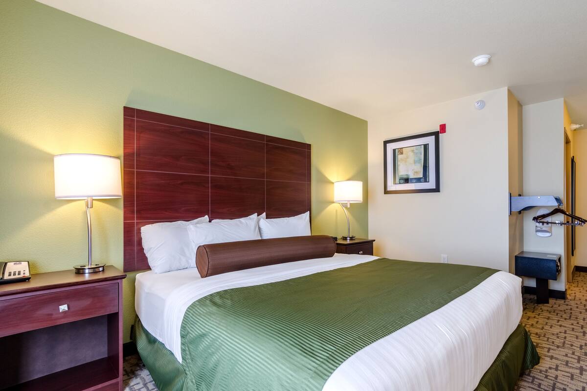 A hotel room with a large bed, two bedside lamps, a wooden headboard, a framed picture on the wall, and a small desk with a telephone.