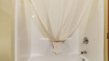 Una bañera con una cortina blanca y una toalla colgando del borde.