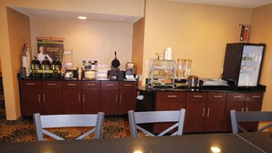 A hotel bar area with wooden cabinets, a counter with various items, and a poster on the wall. - Cobblestone Inn & Suites - Harper (Harper)
