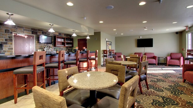 A hotel lobby with a bar area, seating arrangements, and a television mounted on the wall. - Cobblestone Inn & Suites - Harper (Harper)