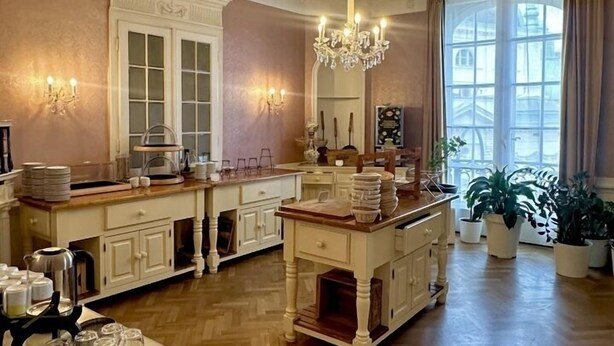 Une cuisine spacieuse dotée d’un îlot central, d’un lustre et d’une grande fenêtre agrémentée de rideaux.
