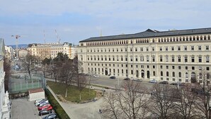 Un grand bâtiment à la façade symétrique, un parking rempli de voitures et un ciel dégagé.