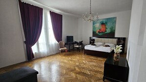 Une chambre d’hôtel avec un parquet en bois disposé en motif chevrons, un lit, un bureau avec une chaise, une télévision et un tableau au mur.