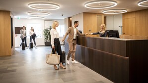 A modern reception area with a wooden reception desk, a ceiling with circular lighting, and a tiled floor. - Hotel Messmer (Bregenz)