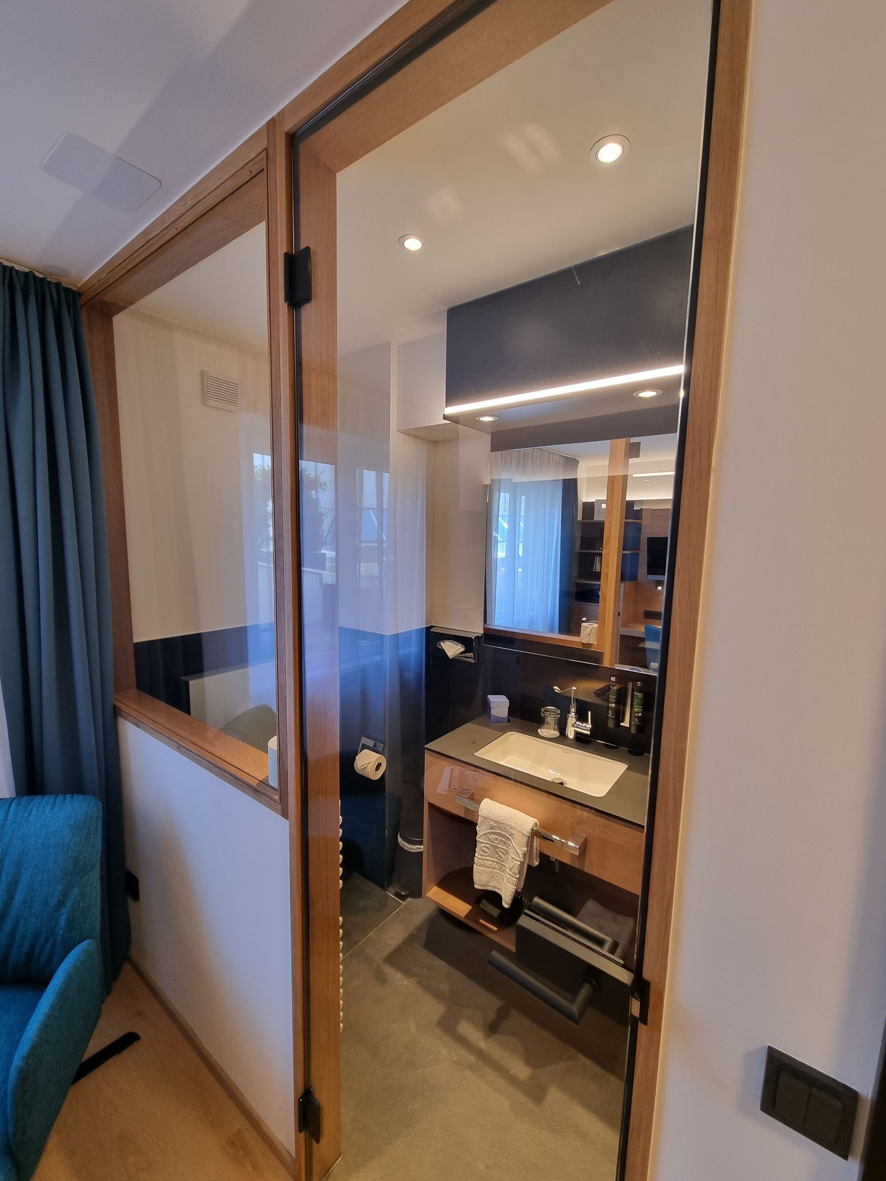 A modern bathroom with a glass partition, a sink, a mirror, and a towel rack.