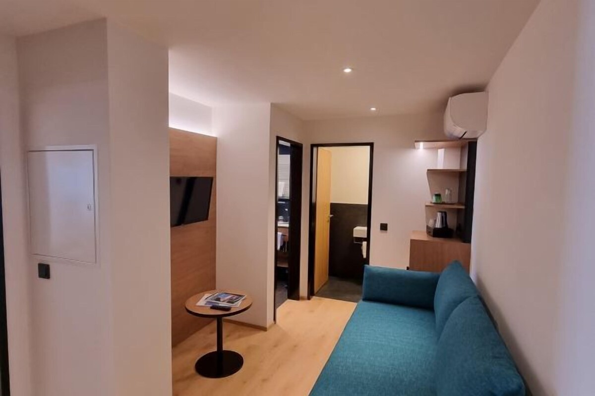 A modern living room with a blue sofa, a small round table with a magazine, and a bookshelf.