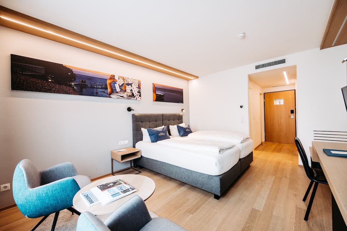 A modern hotel room with a large bed, a desk, and a seating area.
