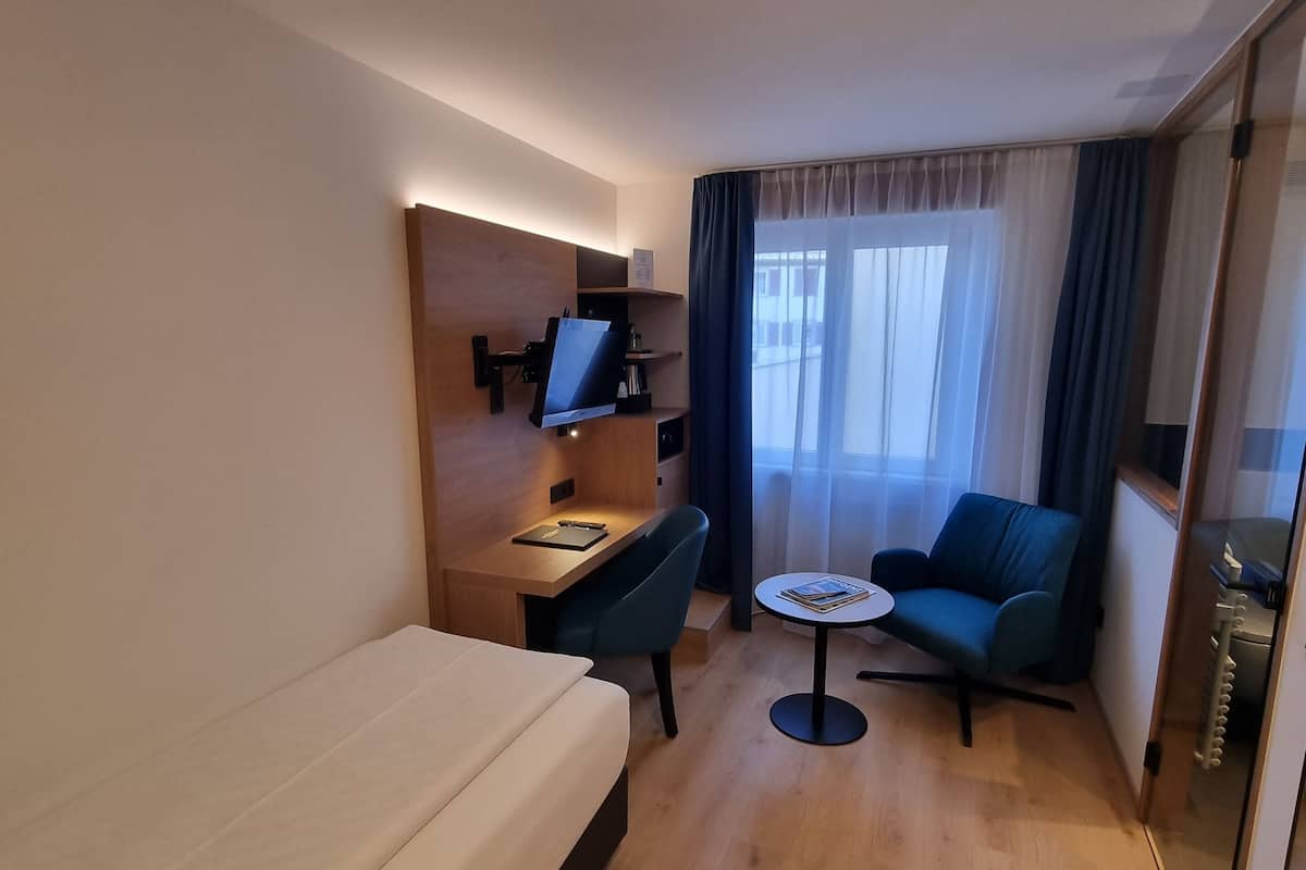 A hotel room with a bed, a desk, a chair, a small table, and a sofa.